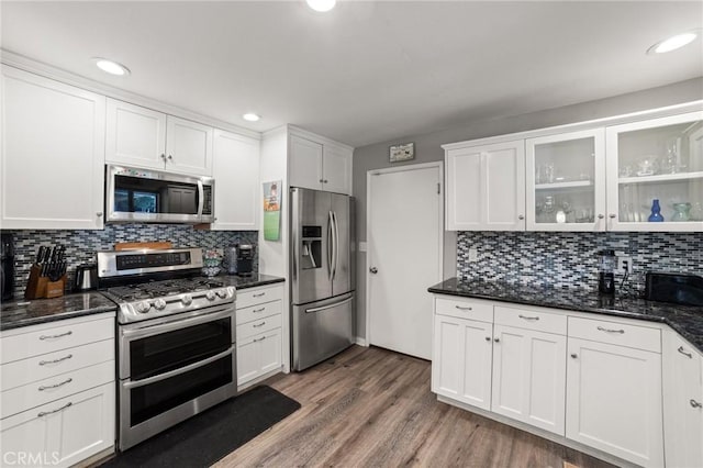 kitchen with white cabinets, dark hardwood / wood-style floors, dark stone countertops, tasteful backsplash, and stainless steel appliances