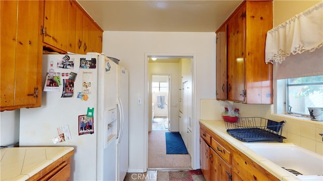 kitchen featuring backsplash, tile countertops, sink, and white refrigerator with ice dispenser