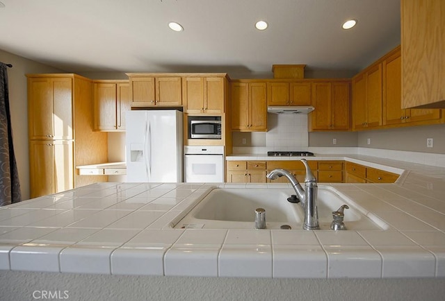 kitchen featuring backsplash, sink, tile counters, and appliances with stainless steel finishes