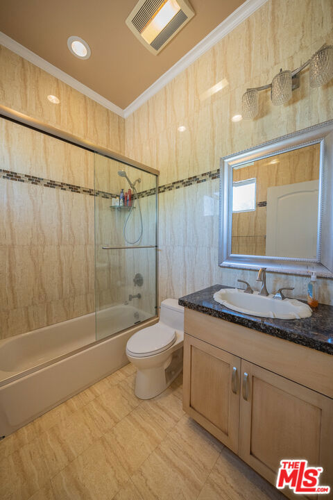 full bathroom featuring shower / bath combination with glass door, vanity, crown molding, and toilet