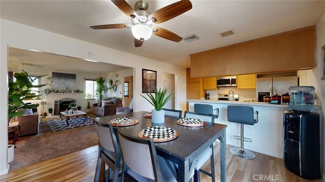 dining room featuring a brick fireplace, a textured ceiling, and light hardwood / wood-style flooring