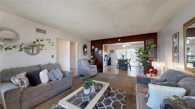 living room featuring carpet, a textured ceiling, ceiling fan, and wood walls