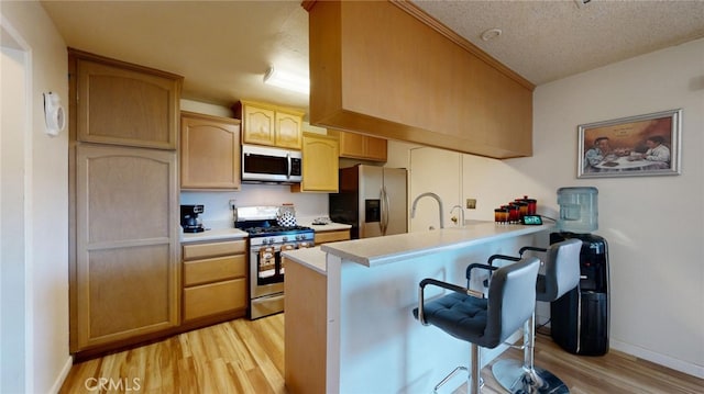 kitchen featuring kitchen peninsula, appliances with stainless steel finishes, a breakfast bar, a textured ceiling, and light hardwood / wood-style flooring