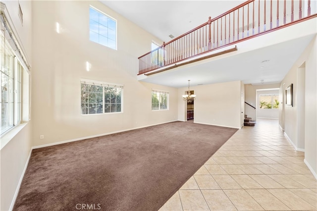 unfurnished living room featuring a chandelier, a towering ceiling, and light colored carpet