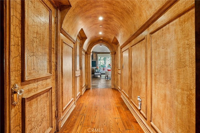 hallway featuring wood walls, hardwood / wood-style floors, and lofted ceiling