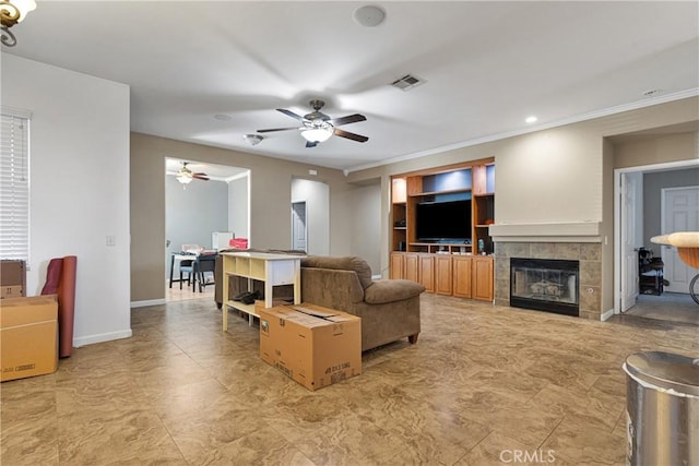 living room featuring a tiled fireplace, ornamental molding, built in features, and ceiling fan