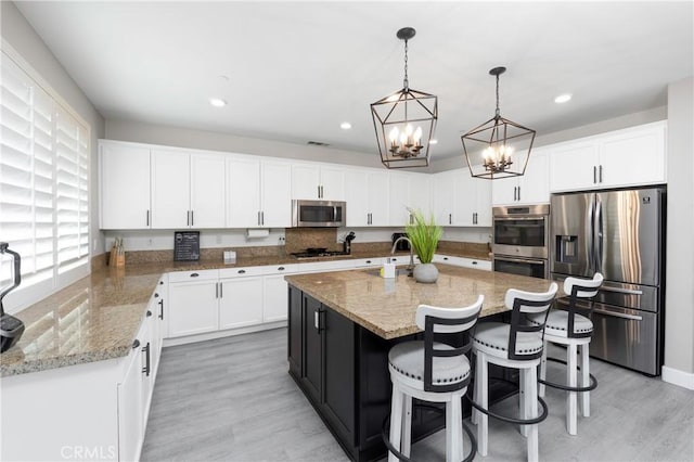 kitchen featuring white cabinets, pendant lighting, appliances with stainless steel finishes, and a kitchen island with sink