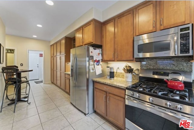 kitchen featuring light stone counters, light tile patterned floors, appliances with stainless steel finishes, and tasteful backsplash