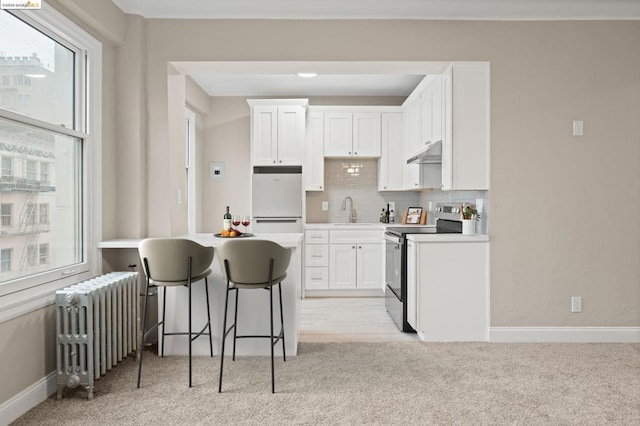 kitchen featuring radiator heating unit, white cabinetry, stainless steel electric range oven, and white fridge