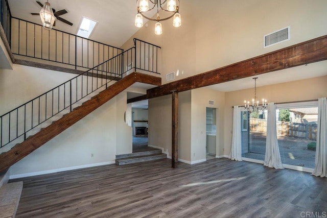 unfurnished living room with a skylight, dark hardwood / wood-style flooring, a towering ceiling, and ceiling fan with notable chandelier