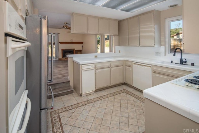 kitchen with light tile patterned floors, kitchen peninsula, white appliances, cream cabinets, and sink