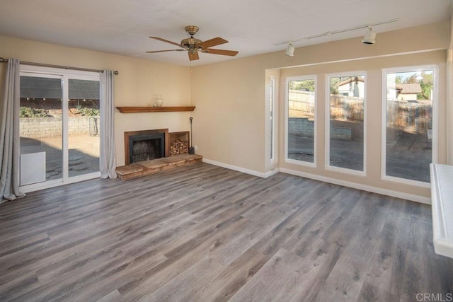 unfurnished living room with ceiling fan, hardwood / wood-style floors, track lighting, and a stone fireplace