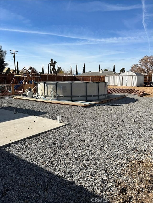 view of yard featuring a storage shed, a playground, a covered pool, and a patio area