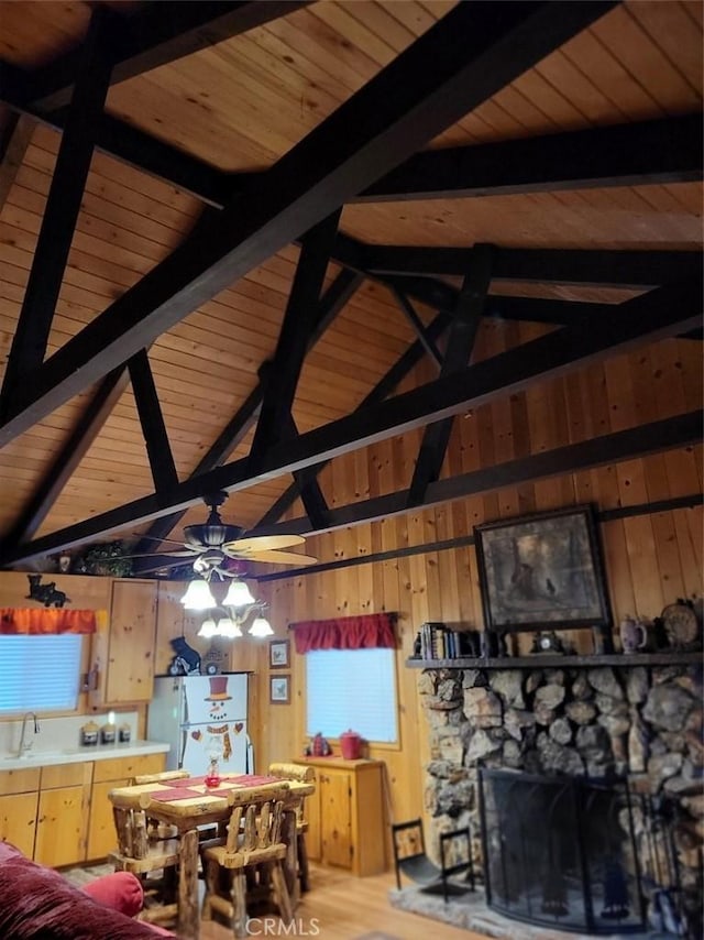 dining room featuring a fireplace, ceiling fan, wooden walls, high vaulted ceiling, and beamed ceiling