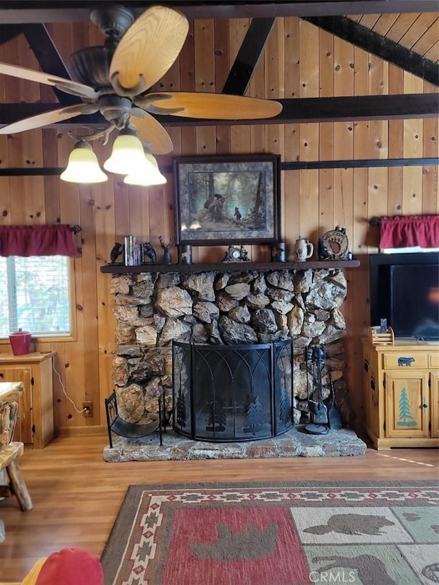 living room featuring ceiling fan, a stone fireplace, vaulted ceiling with beams, wood-type flooring, and wooden walls