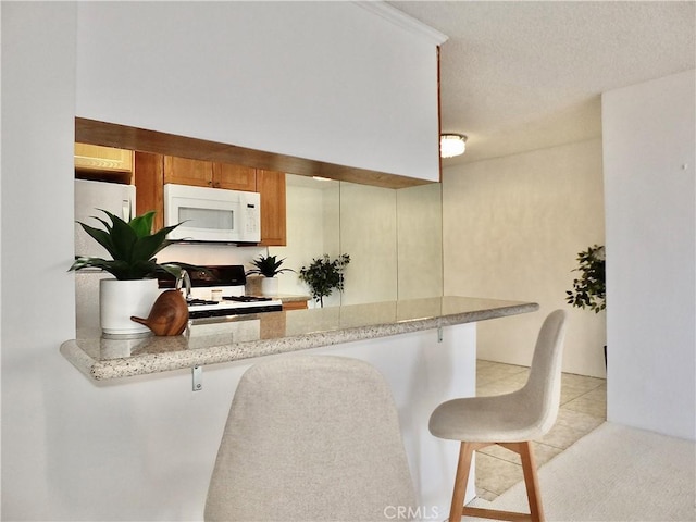 kitchen featuring a breakfast bar area, stove, light tile patterned floors, kitchen peninsula, and light stone countertops