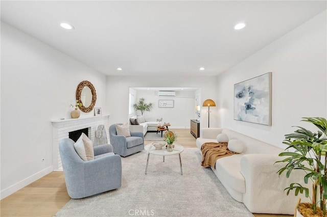 living room with light wood-type flooring, a wall mounted AC, and a fireplace