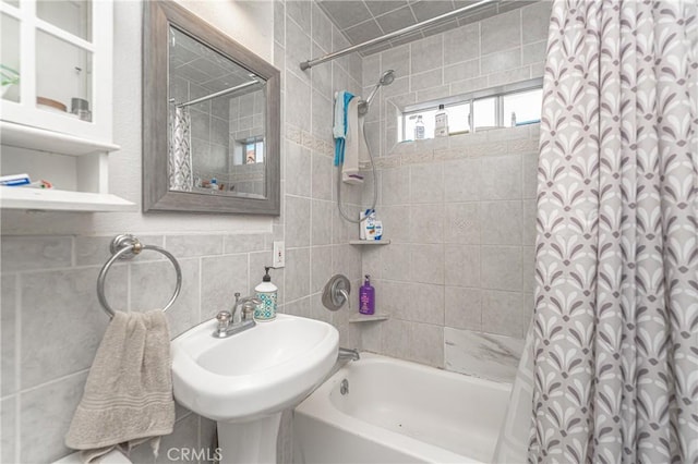 bathroom featuring backsplash, tile walls, shower / bath combo with shower curtain, and sink