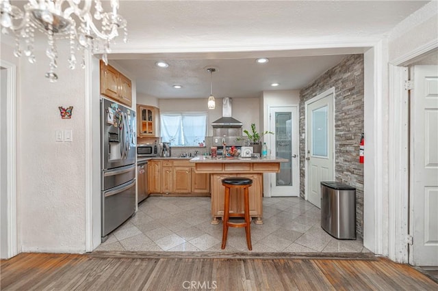 kitchen featuring a breakfast bar, wall chimney range hood, hanging light fixtures, light hardwood / wood-style flooring, and appliances with stainless steel finishes