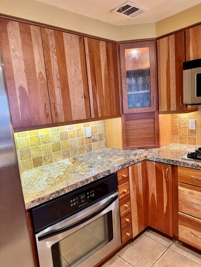 kitchen with light stone countertops, appliances with stainless steel finishes, tasteful backsplash, and light tile patterned flooring