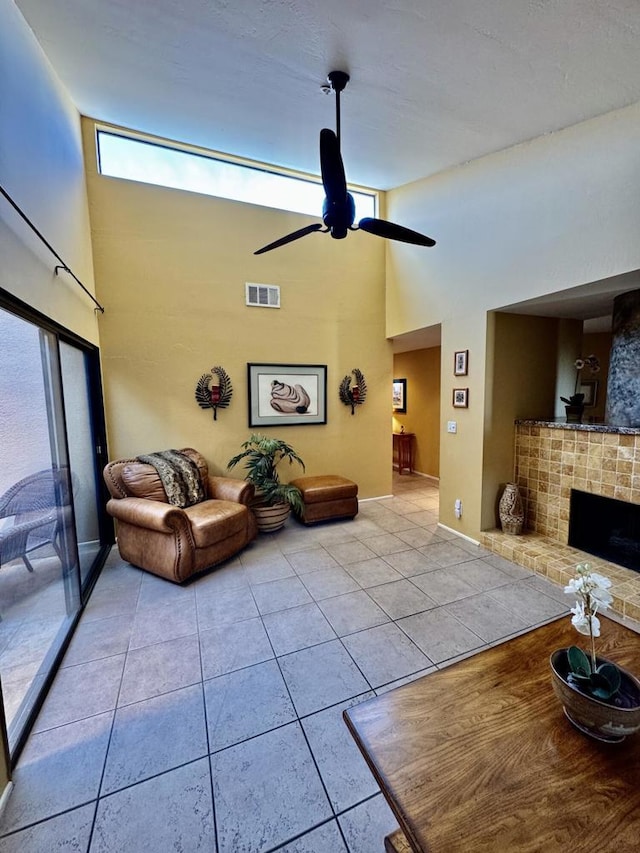 tiled living room featuring ceiling fan, a towering ceiling, and a fireplace