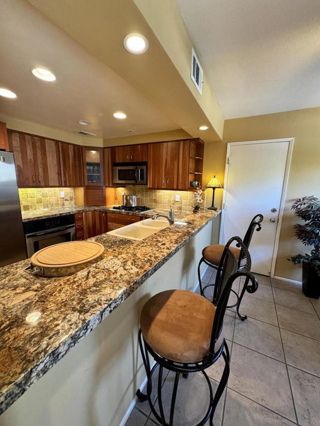 kitchen featuring kitchen peninsula, backsplash, stainless steel appliances, light tile patterned floors, and stone countertops