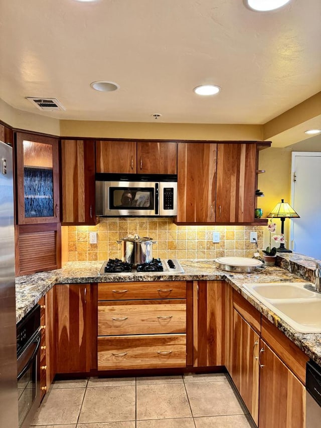 kitchen featuring backsplash, sink, light stone countertops, appliances with stainless steel finishes, and light tile patterned flooring