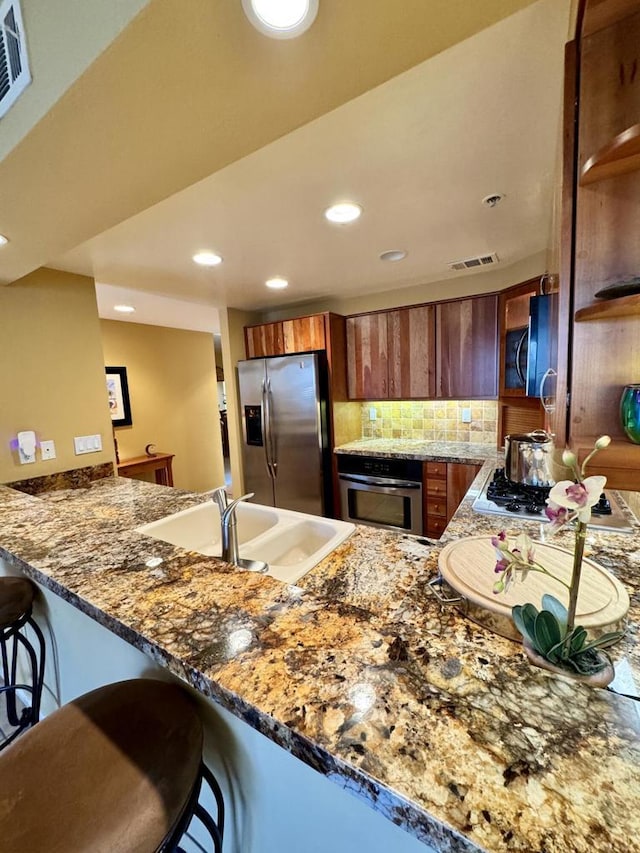 kitchen with tasteful backsplash, kitchen peninsula, dark stone countertops, a breakfast bar area, and appliances with stainless steel finishes