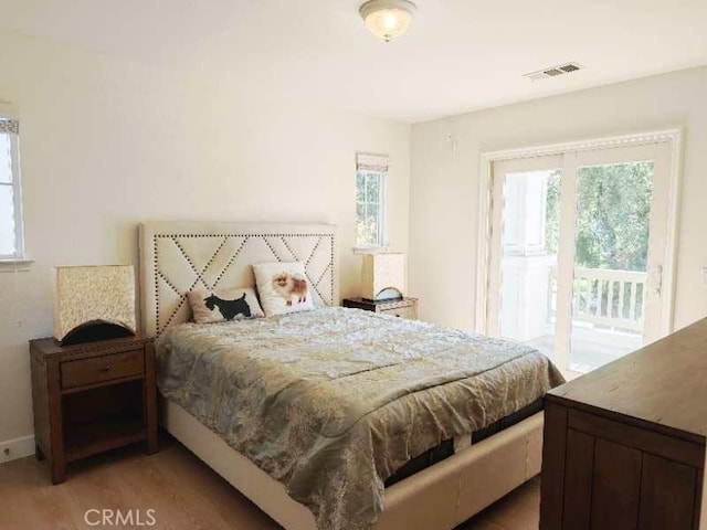 bedroom with wood-type flooring, access to outside, and multiple windows