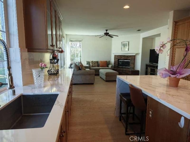 kitchen featuring light stone countertops, wood-type flooring, a stone fireplace, and ceiling fan