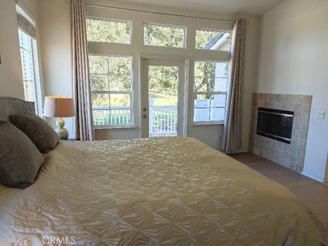 bedroom featuring a tiled fireplace, access to exterior, and multiple windows