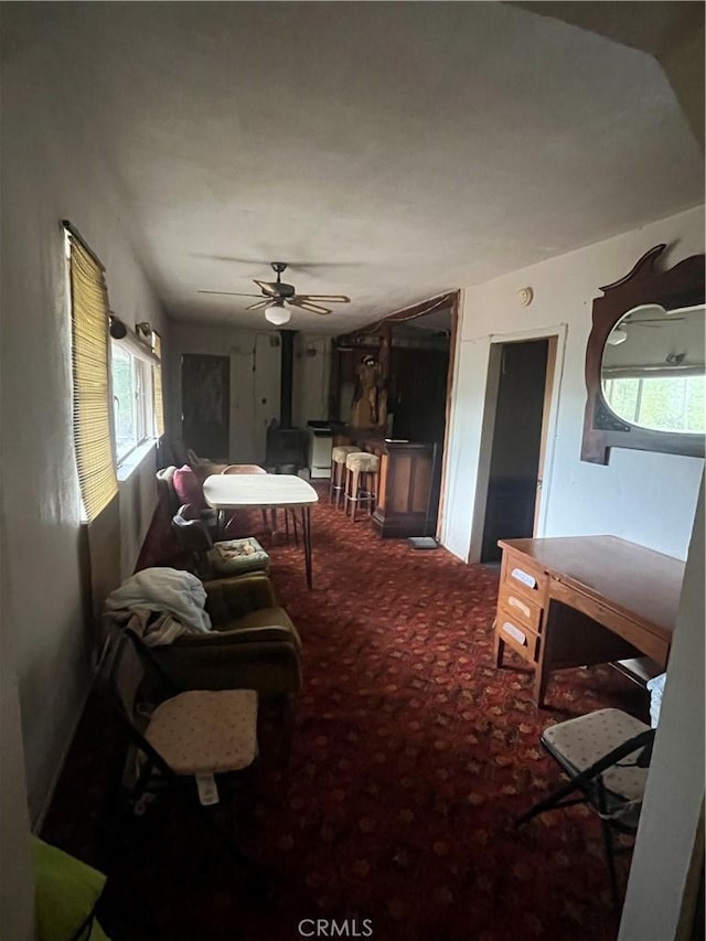 living area with carpet floors, a ceiling fan, a healthy amount of sunlight, and a wood stove