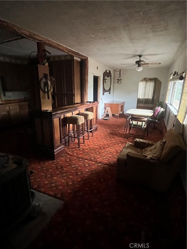 carpeted living room with a textured ceiling, ceiling fan, and a wood stove