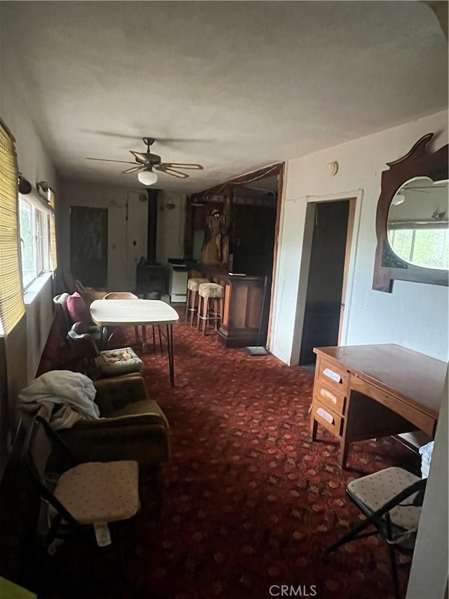 living room featuring carpet, a wood stove, a healthy amount of sunlight, and ceiling fan