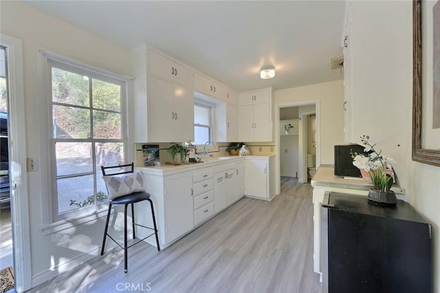 kitchen with white cabinets, a kitchen bar, light wood-type flooring, and sink