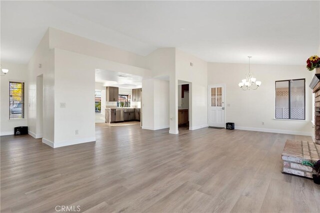 unfurnished living room with a brick fireplace, light hardwood / wood-style flooring, an inviting chandelier, and lofted ceiling