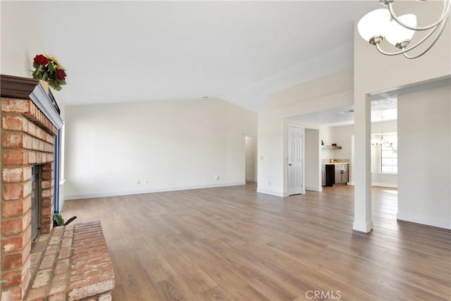 unfurnished living room with a notable chandelier, hardwood / wood-style floors, a brick fireplace, and vaulted ceiling