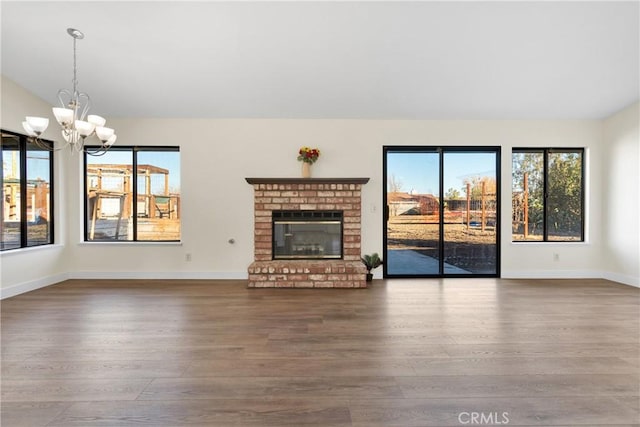 unfurnished living room featuring a brick fireplace, an inviting chandelier, and hardwood / wood-style floors