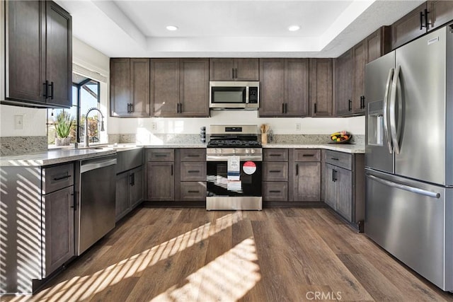 kitchen featuring stainless steel appliances, sink, a raised ceiling, dark brown cabinets, and dark wood-type flooring