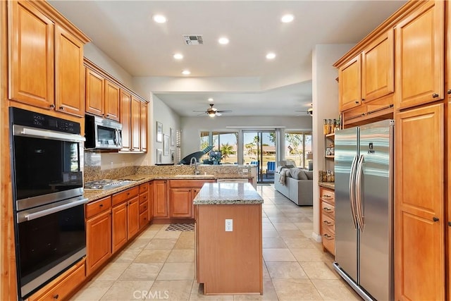 kitchen with ceiling fan, a kitchen island, sink, light stone countertops, and stainless steel appliances