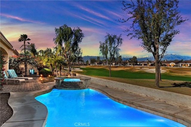 pool at dusk featuring a patio area, a yard, and an in ground hot tub