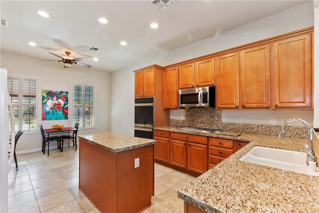 kitchen featuring light stone countertops, a kitchen island, stainless steel appliances, sink, and ceiling fan