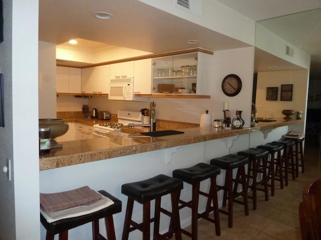 kitchen with white appliances, white cabinets, tile patterned flooring, kitchen peninsula, and a breakfast bar area