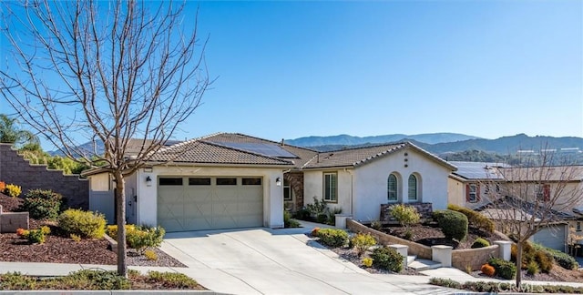 view of front of property with stucco siding, solar panels, an attached garage, a mountain view, and driveway