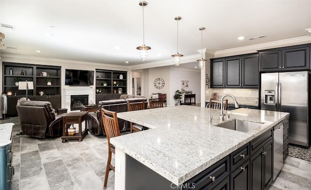 kitchen with sink, hanging light fixtures, stainless steel appliances, light stone countertops, and a kitchen island with sink