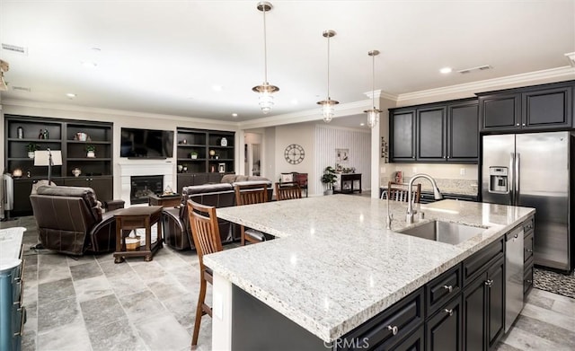 kitchen featuring stainless steel appliances, a sink, visible vents, hanging light fixtures, and a center island with sink