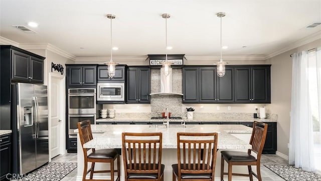 kitchen featuring a breakfast bar, hanging light fixtures, a kitchen island with sink, appliances with stainless steel finishes, and wall chimney exhaust hood