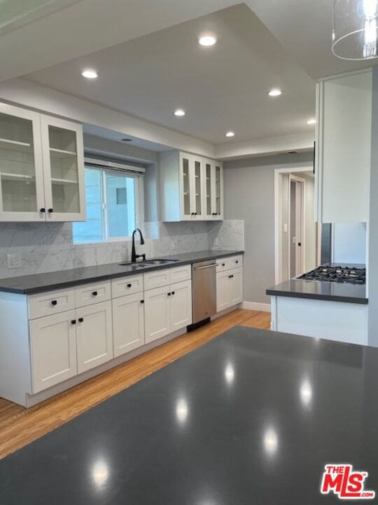 kitchen with tasteful backsplash, sink, white cabinetry, light wood-type flooring, and appliances with stainless steel finishes