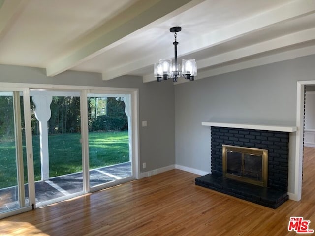 unfurnished living room featuring a brick fireplace, beamed ceiling, hardwood / wood-style flooring, and a notable chandelier