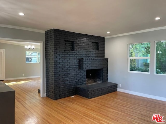 unfurnished living room with a fireplace, an inviting chandelier, ornamental molding, and light hardwood / wood-style floors